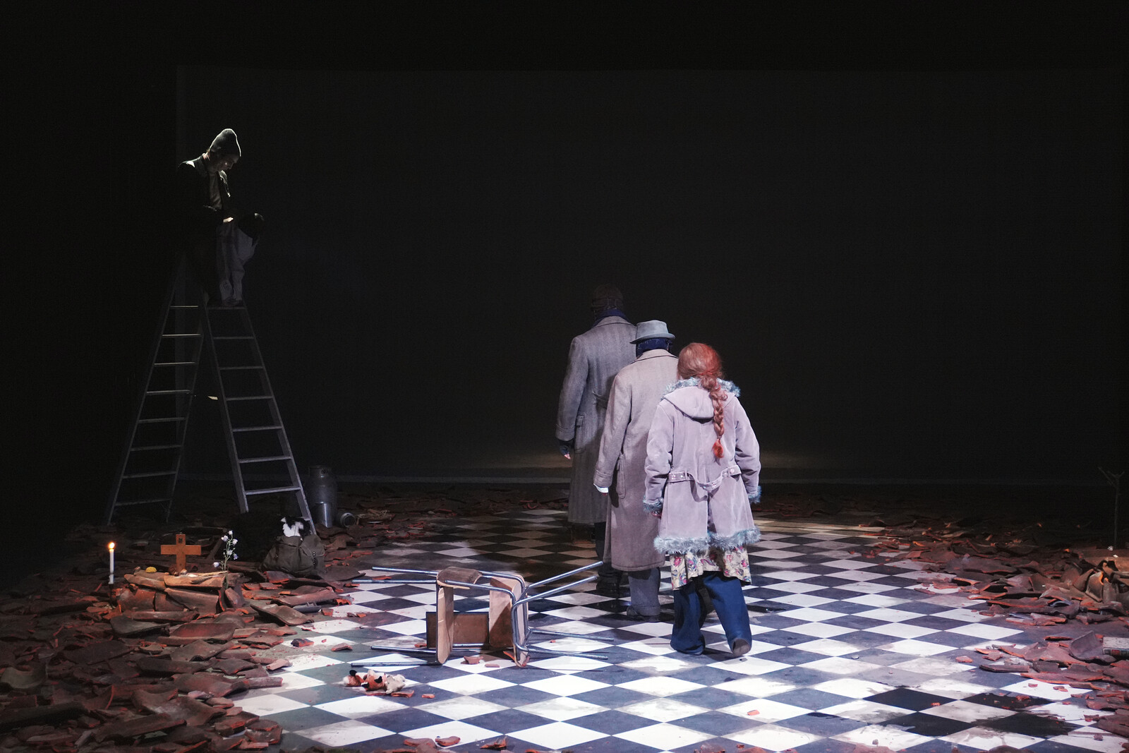 Rubble, roof tiles, a checkerboard floor, three actors turn away and leave.