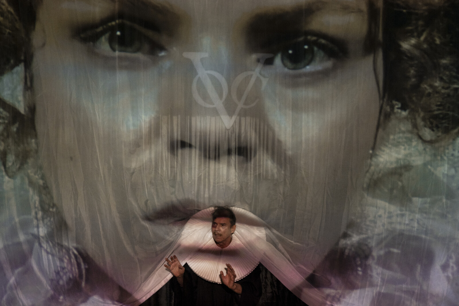 Eve's face is projected large onto a gauze, with Judge Adam peering out from underneath.