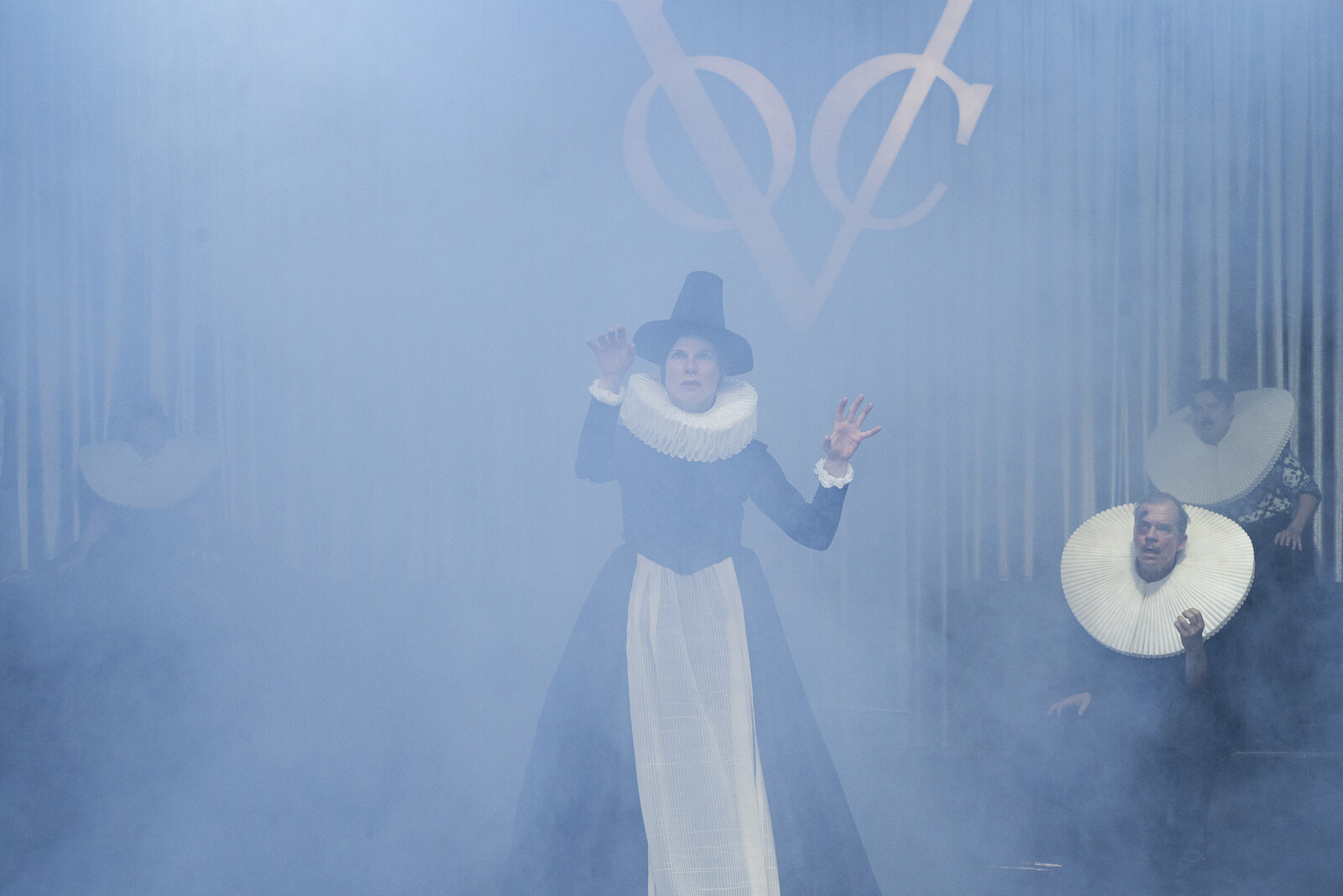 Mrs Brigitte stands gesticulating in the fog and speaks, while Adam and Ruprecht listen in the background.