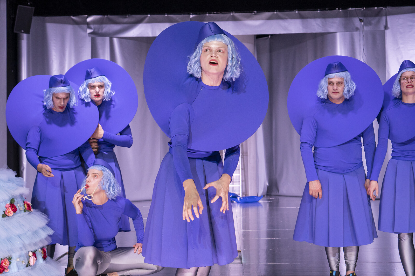 An actress dressed in blue delivers a monologue while the other actors listen to her.