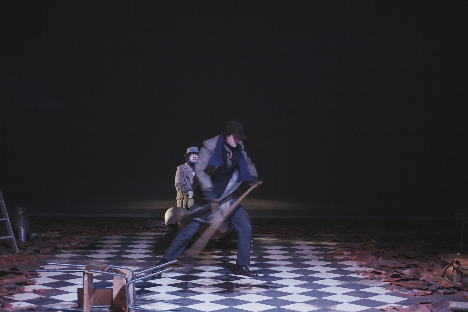 A man is swinging a scythe; behind him, a person is sitting next to a church bell lying on the ground.