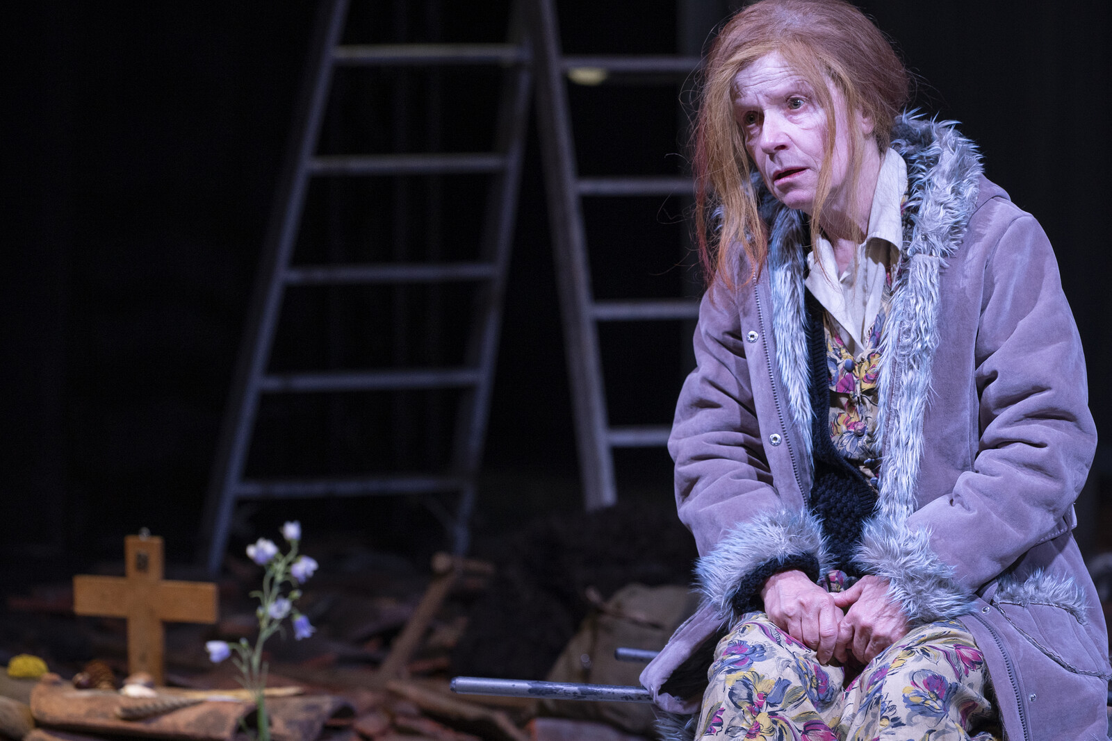 A woman is sitting in front of a ladder; she has red hair