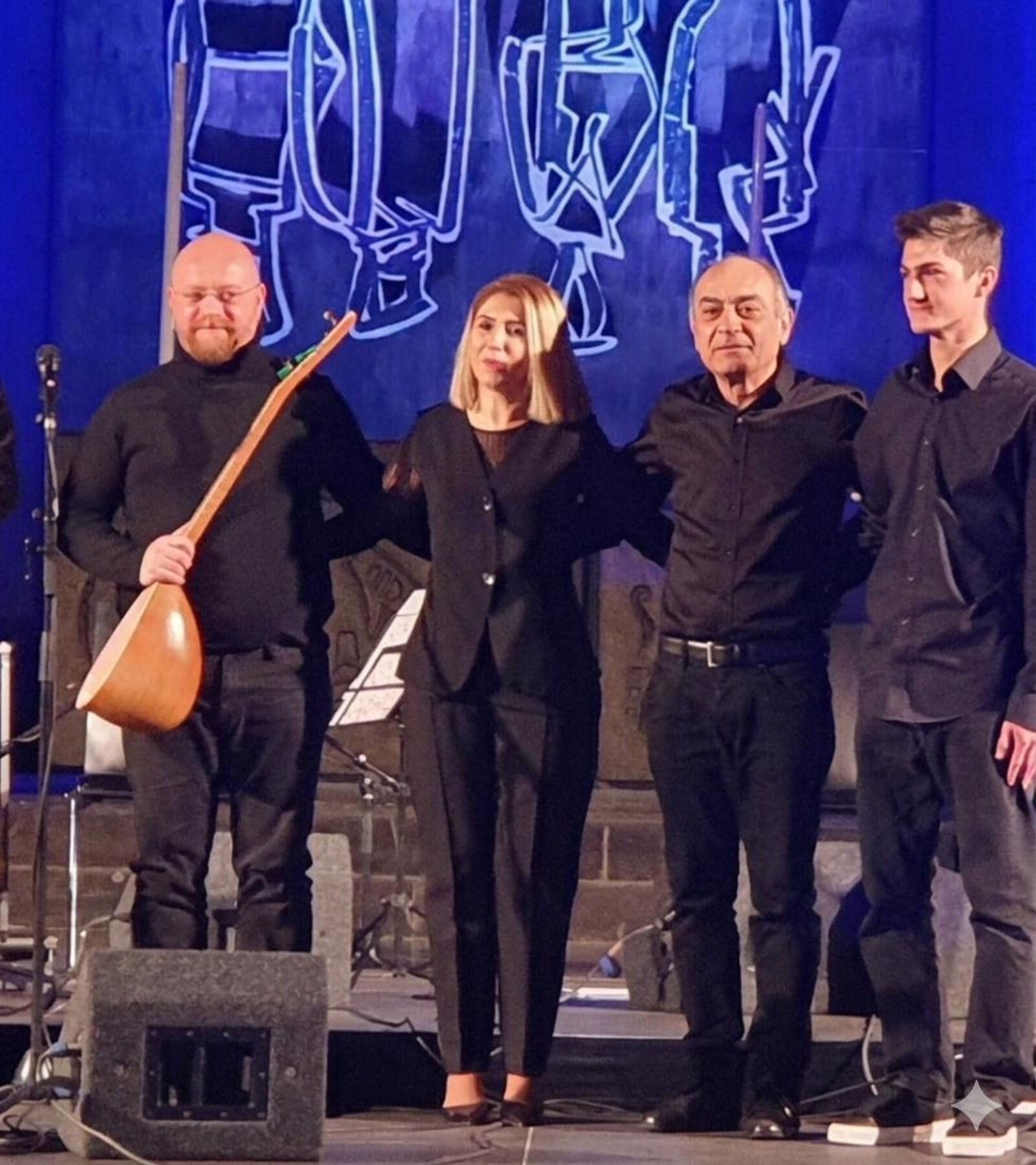 vier musiker*innen stehen auf der bühne mit gitarre beim applaus in schwarz gekleidet