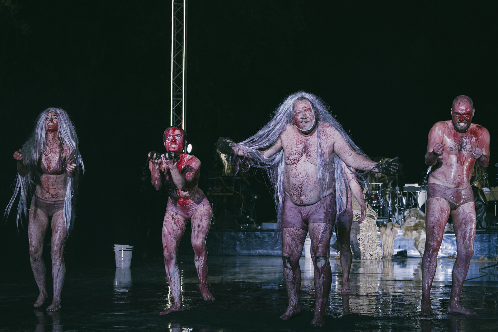 Eine Gruppe nackter, mit roter Farbe beschmierter Schauspieler ruft ins Publikum.