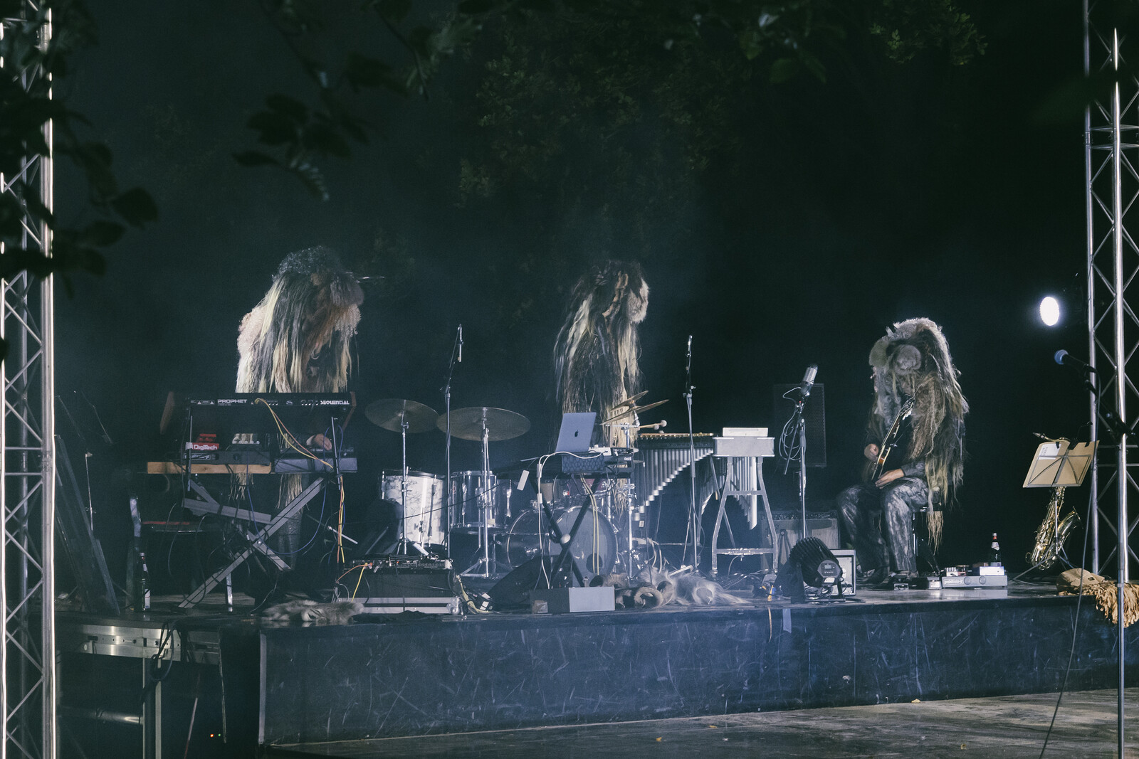 Die drei Musiker mit übergroßen Masken auf ihren Köpfen im Nebel an ihren Instrumenten.