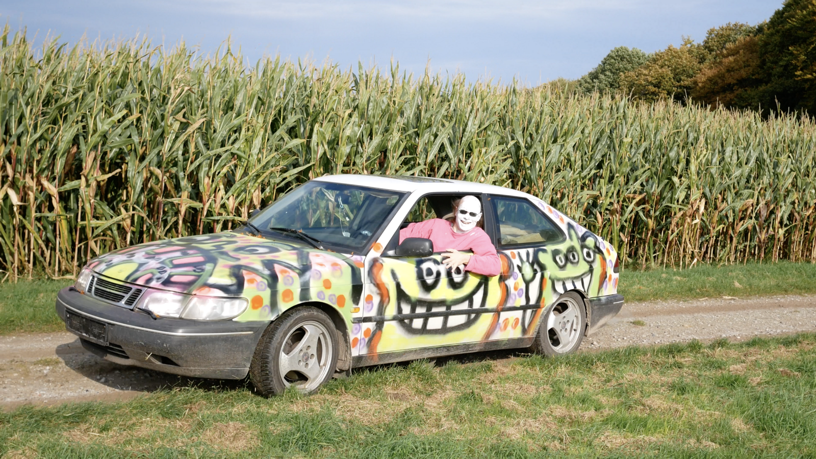 DJ Hundefriedhof in einem mit graffiti besprühten auto vor einem maisfeld