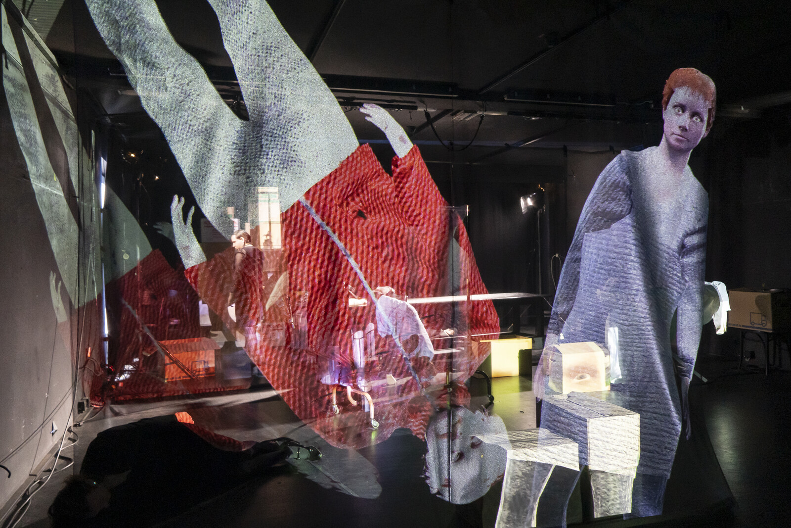 Projektionen von Menschen auf Gaze in einem abgedunkelten Raum, im Hintergrund steht ein Mann am Fenster.