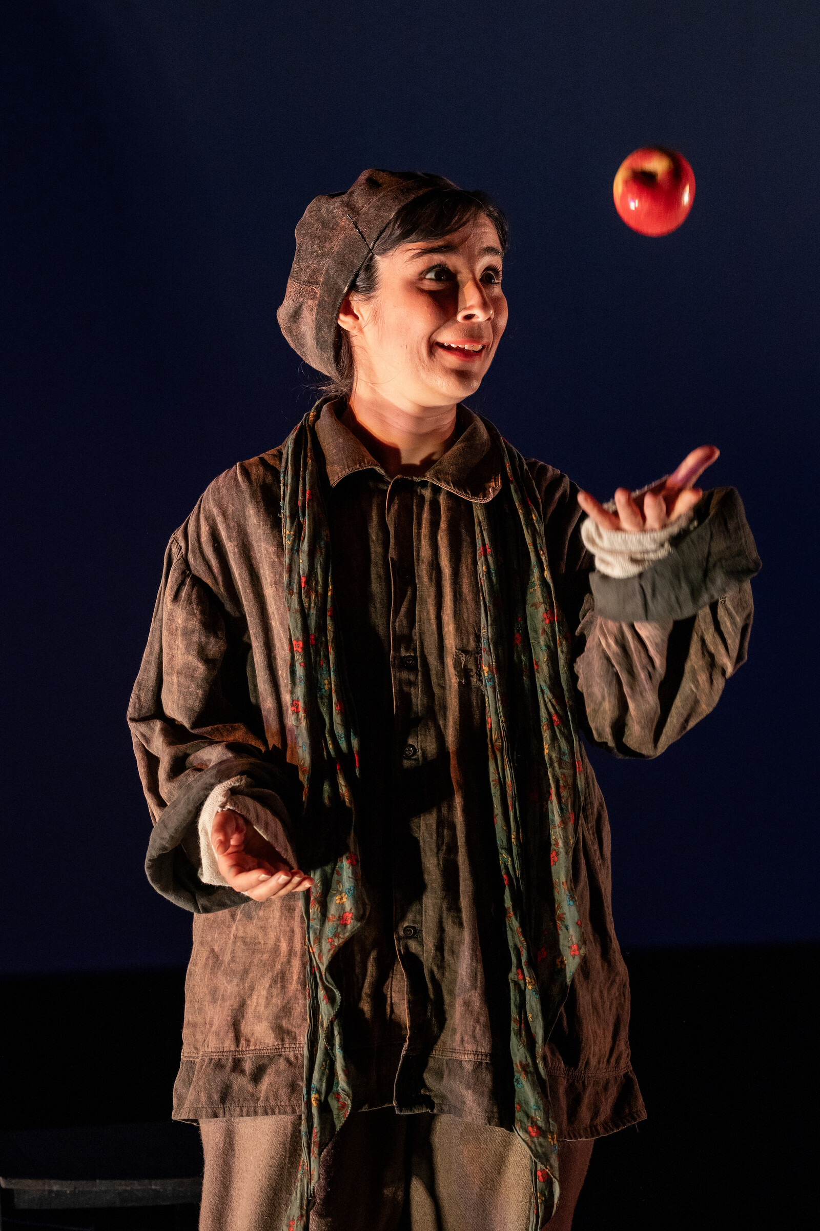 a women with a hat wearing androgyn clothes juggles an apple