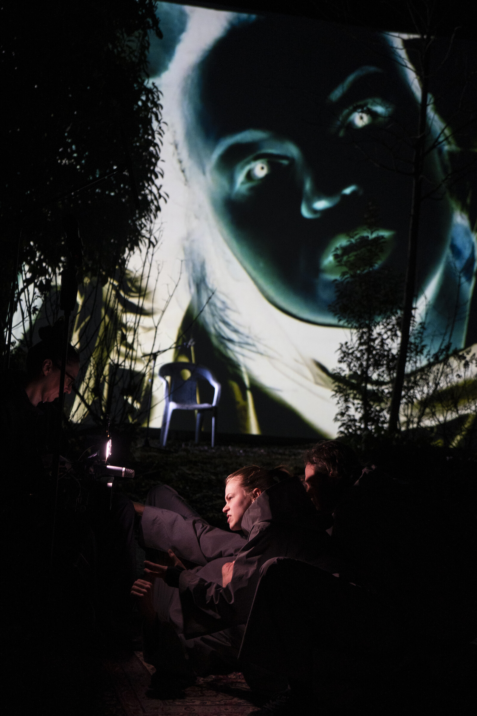 Eine Frau schaut im Dunkeln in eine Kamera, ihr Gesicht wird in Negativfarben auf den Hintergrund projiziert.