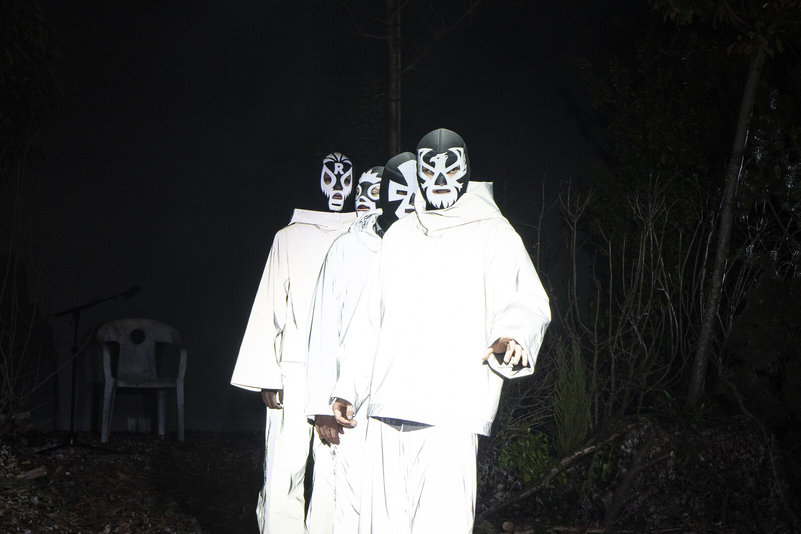 Vier Darsteller mit Wrestling-Masken und reflektierender Kleidung stehen hintereinander in einer Reihe.