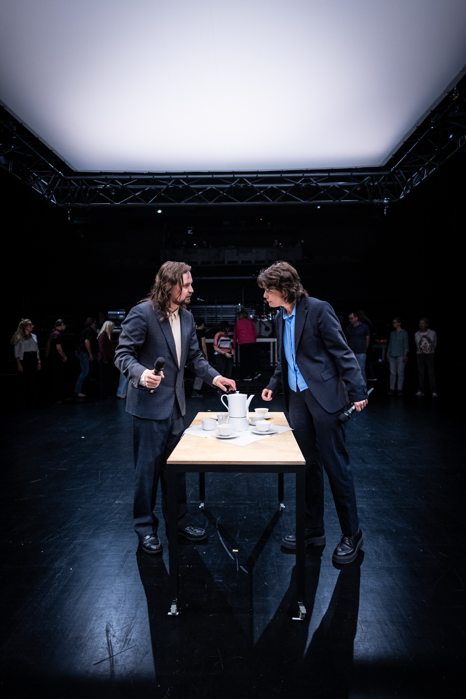 Two people in suits stand facing each other at a table.