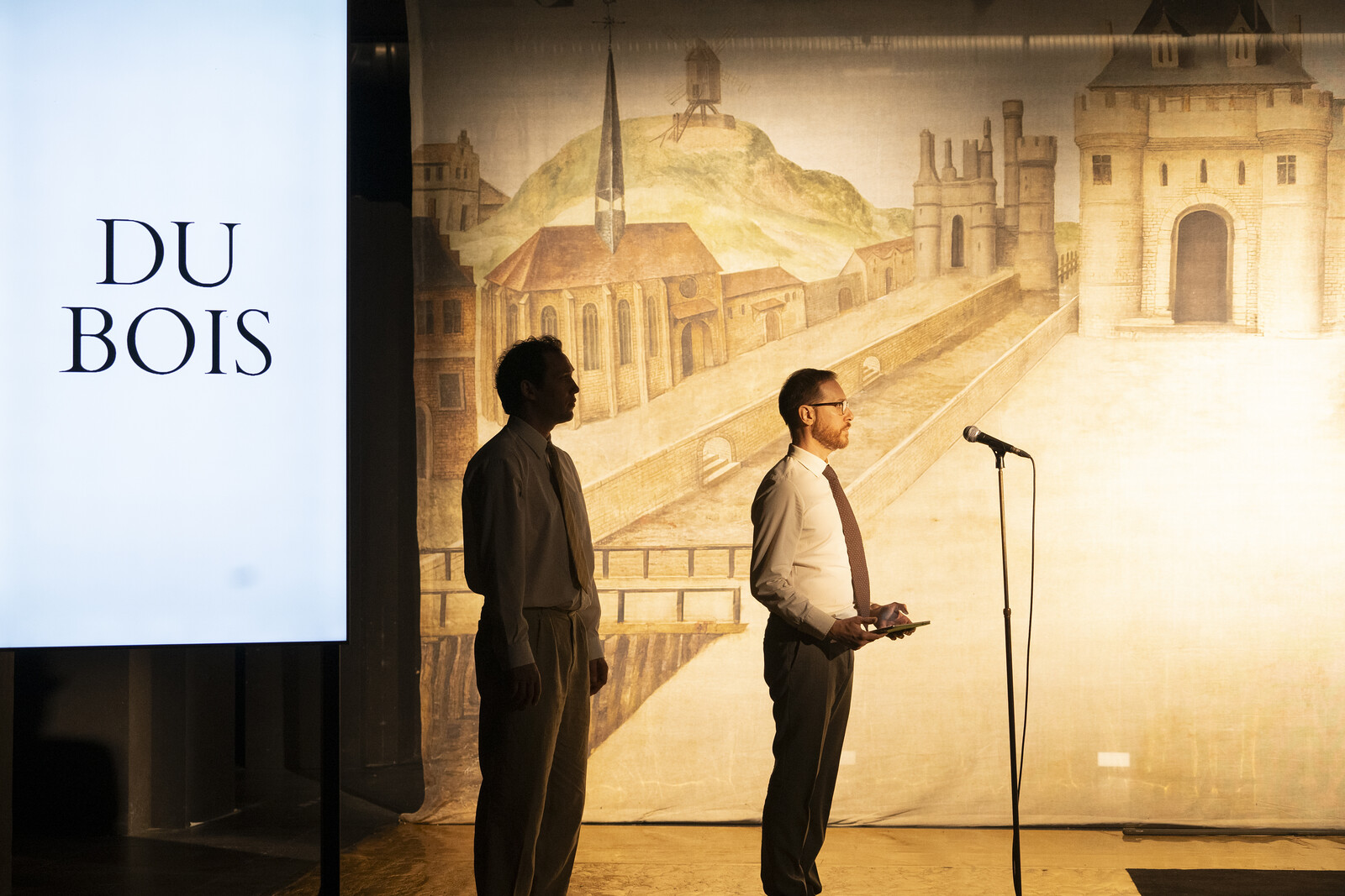 Two men with ties are standing on the stage, next to them the name Du Bois is displayed on a monitor.
