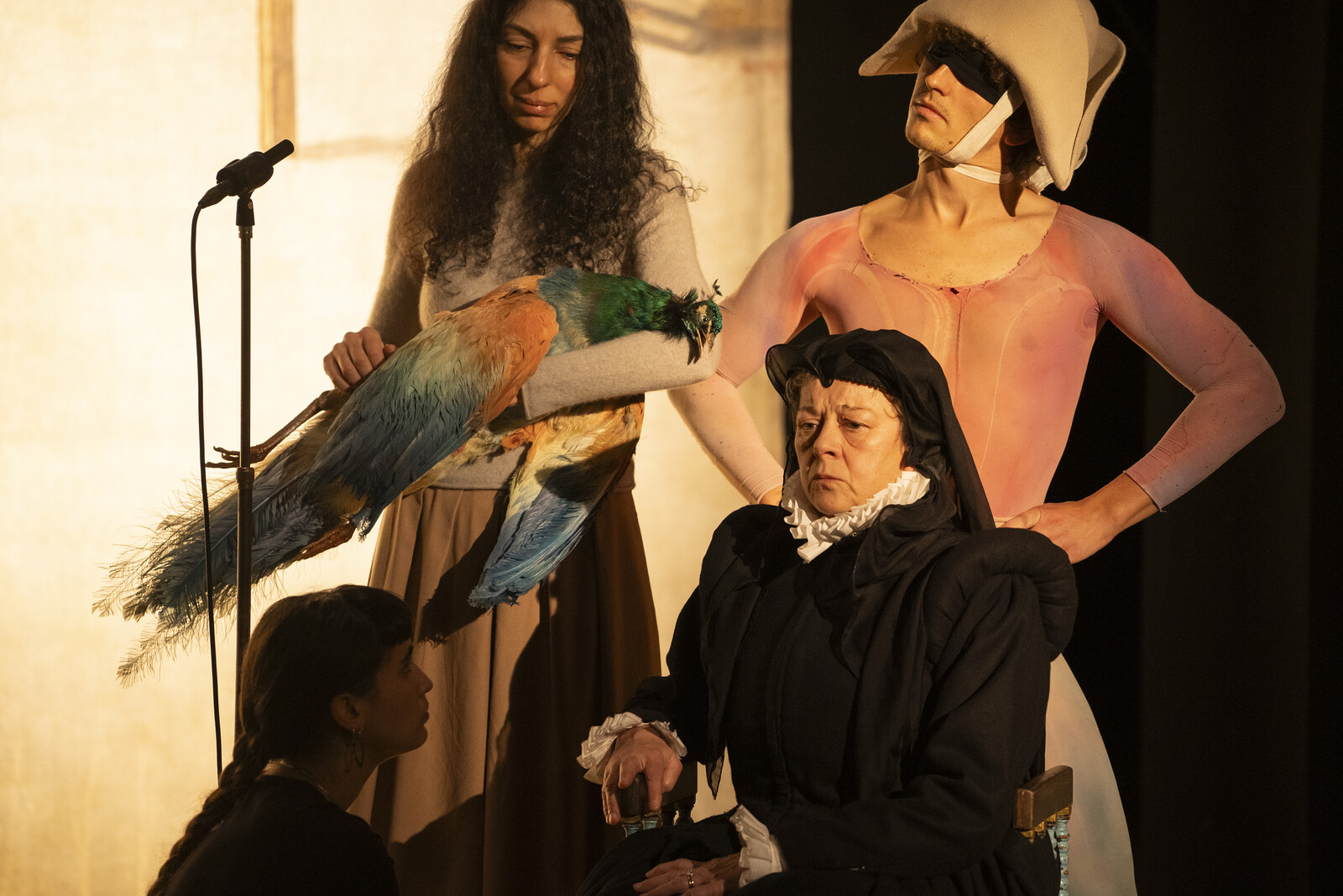 A woman with a bird, a jester, a woman in the shadows and a woman dressed in black as a group on stage