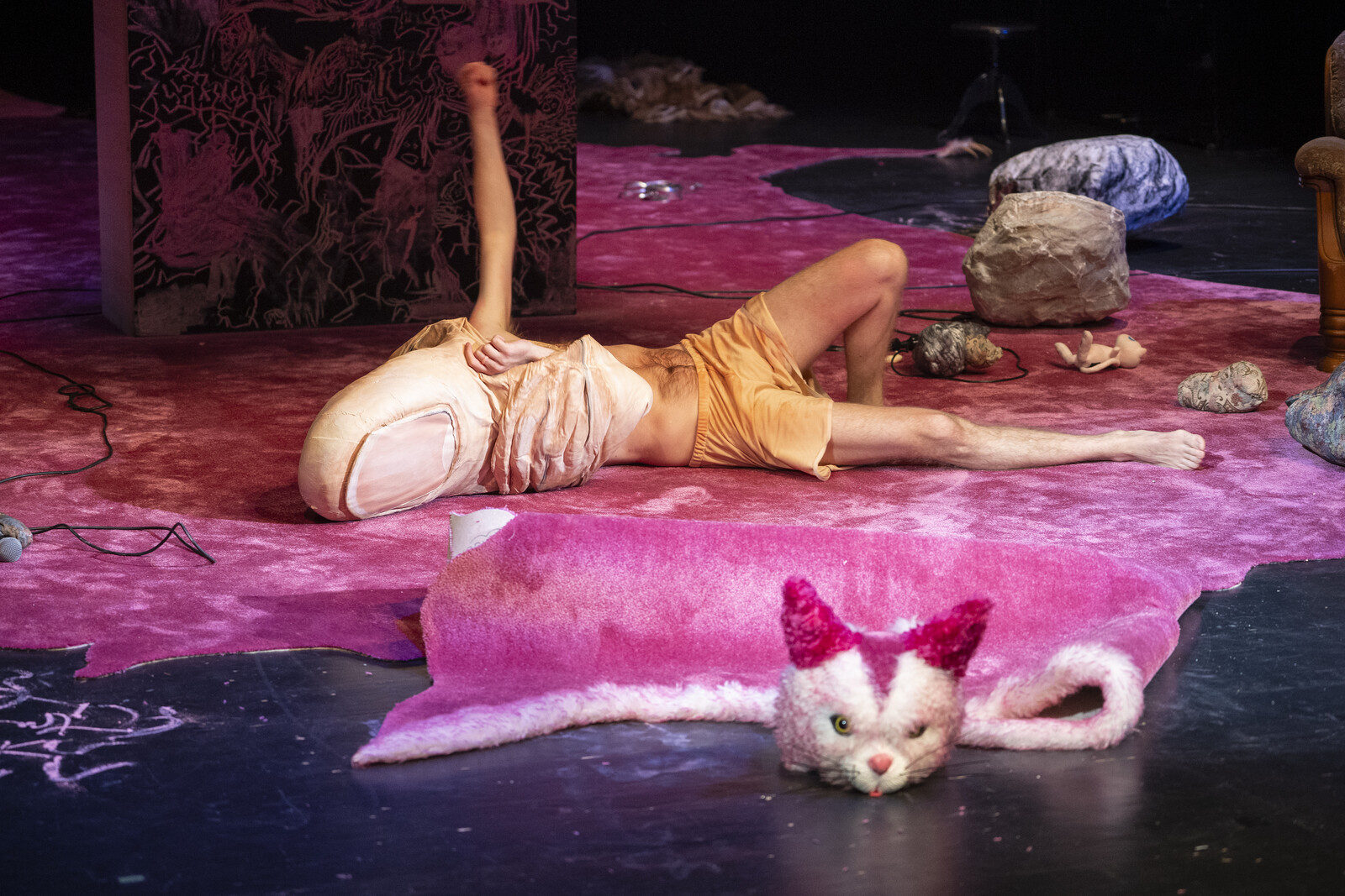 The actor lies on a pink carpet wearing a thumb costume.