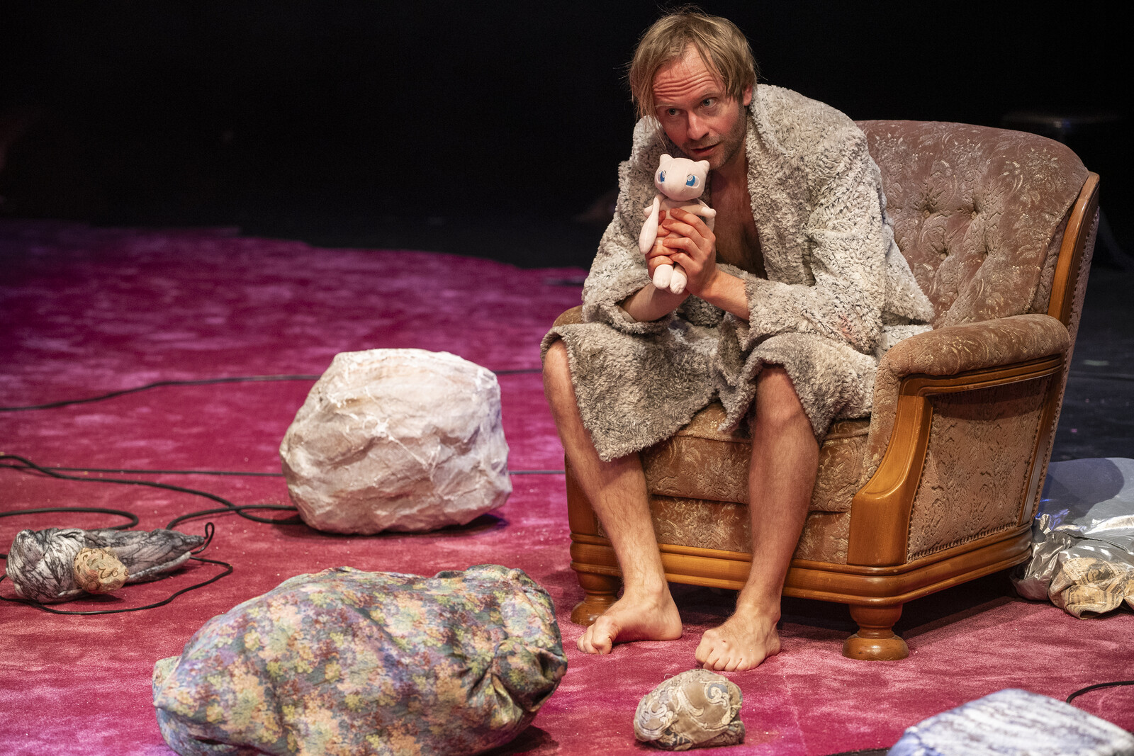 The actor sits on an old armchair and holds a Pokémon doll.