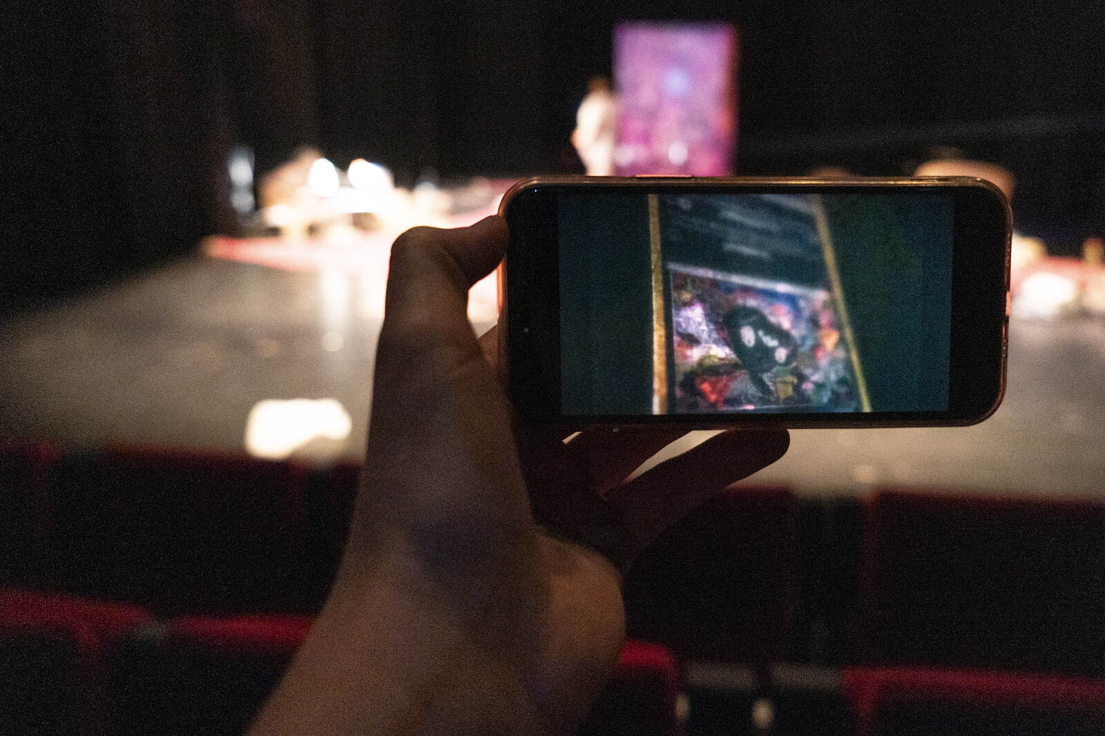 In front of the stage, someone holds up a mobile phone displaying another image.