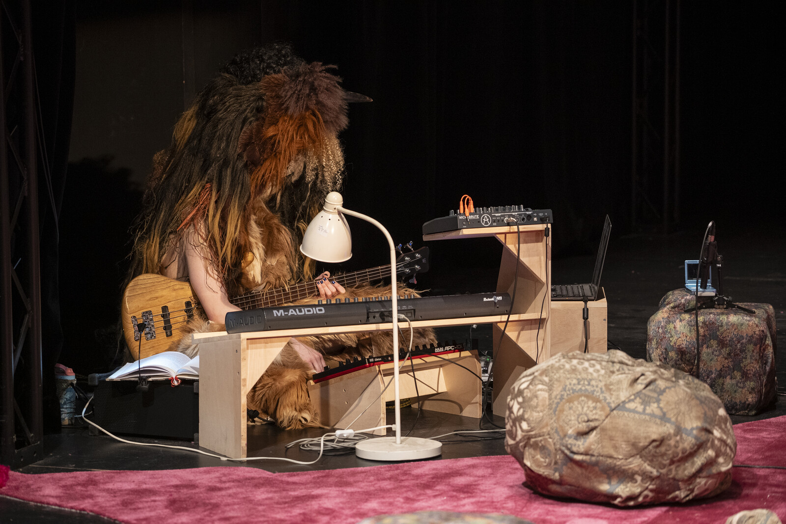 A musician wearing a huge fur mask sits behind a keyboard with a guitar. 