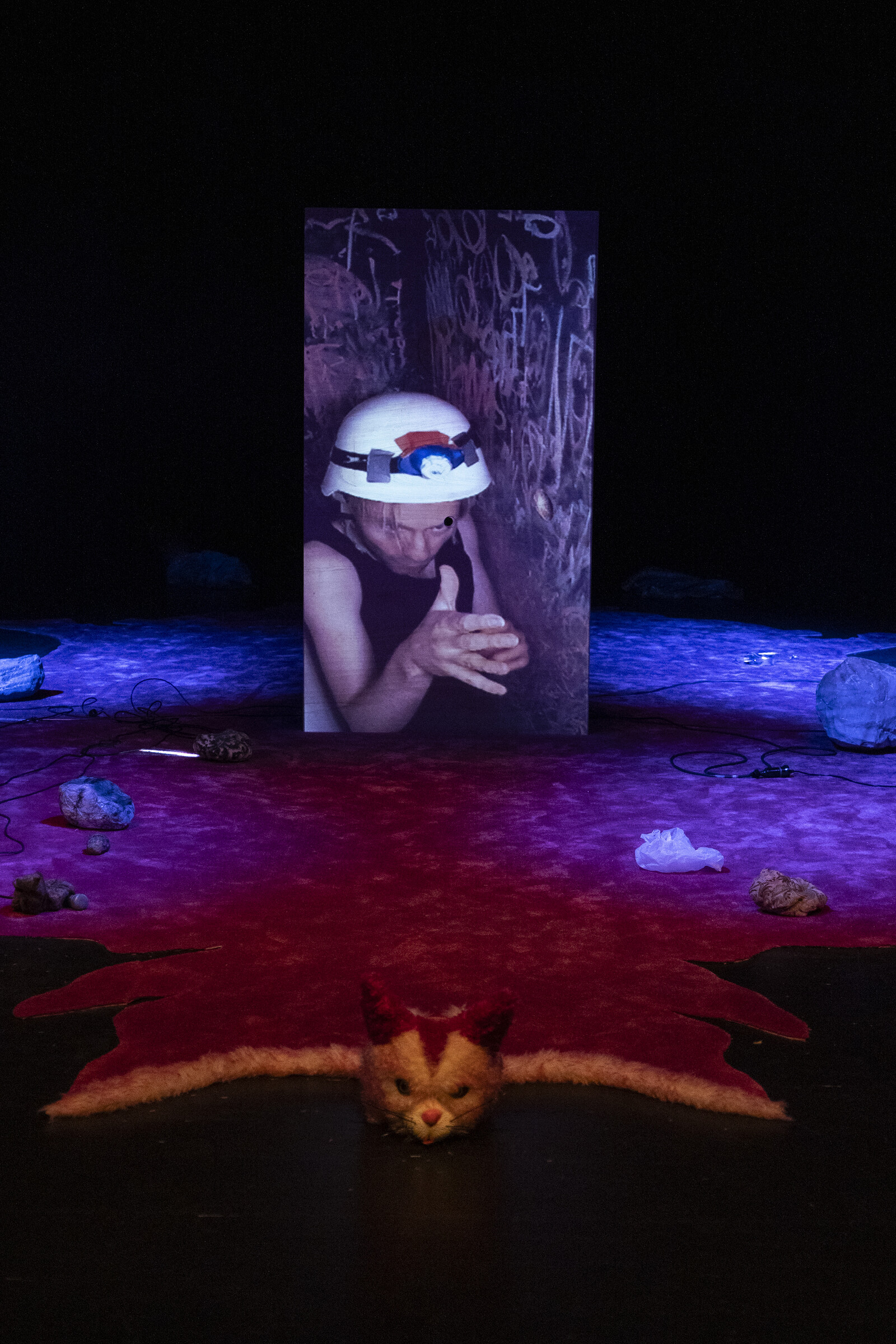 The image of the actor wearing an illuminated safety helmet is projected onto a large wooden box.