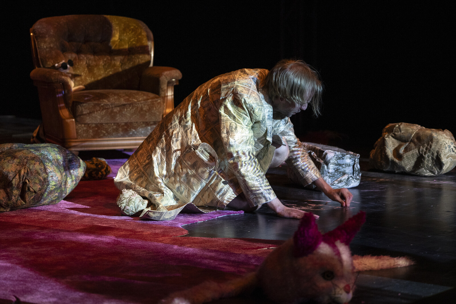 The actor, dressed in a coat, is crouching on the floor and drawing something with chalk.