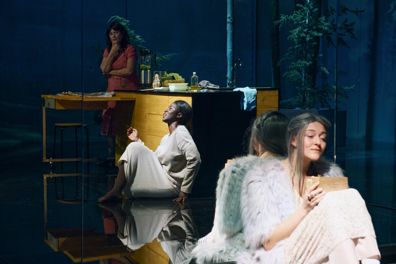 Frau sitzt auf dem Boden, hinter ihr ein Spiegel, auf der Bühne es ist Dunkel