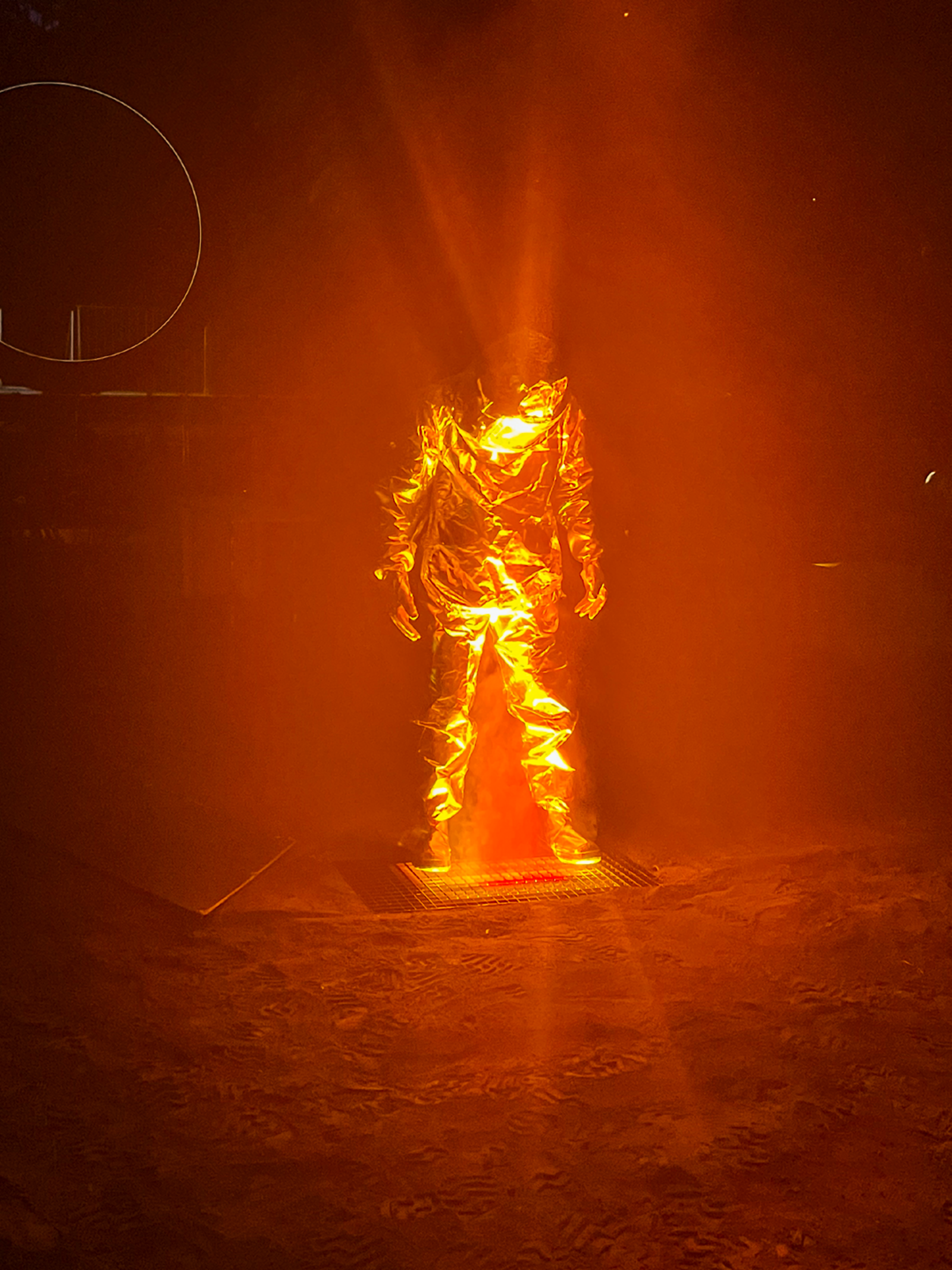 A person wearing a fire-resistant suit is standing in a stage fire.
