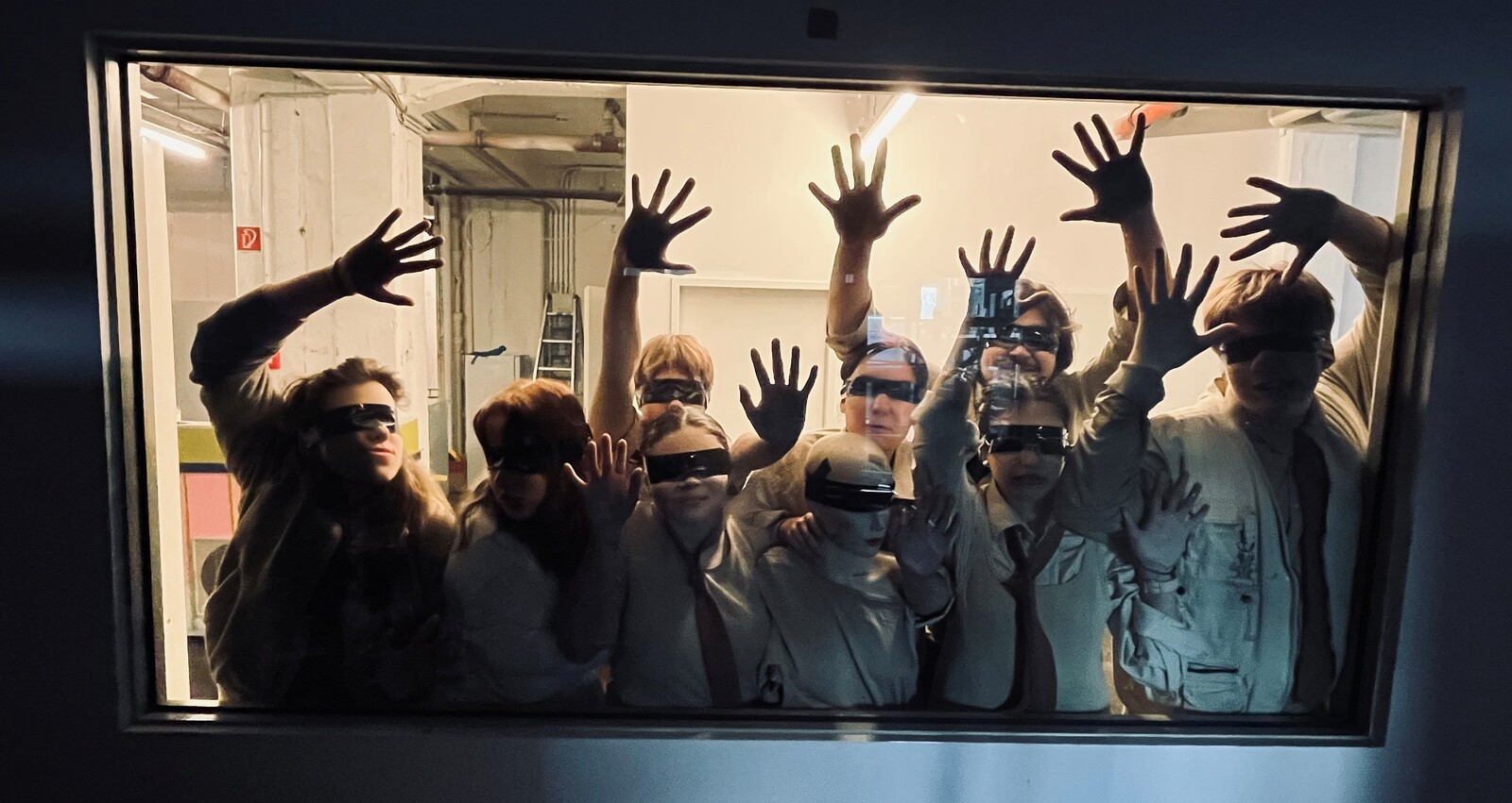 Viele junge Menschen stehe hinter einer Scheibe, die Hände an dem Fenster