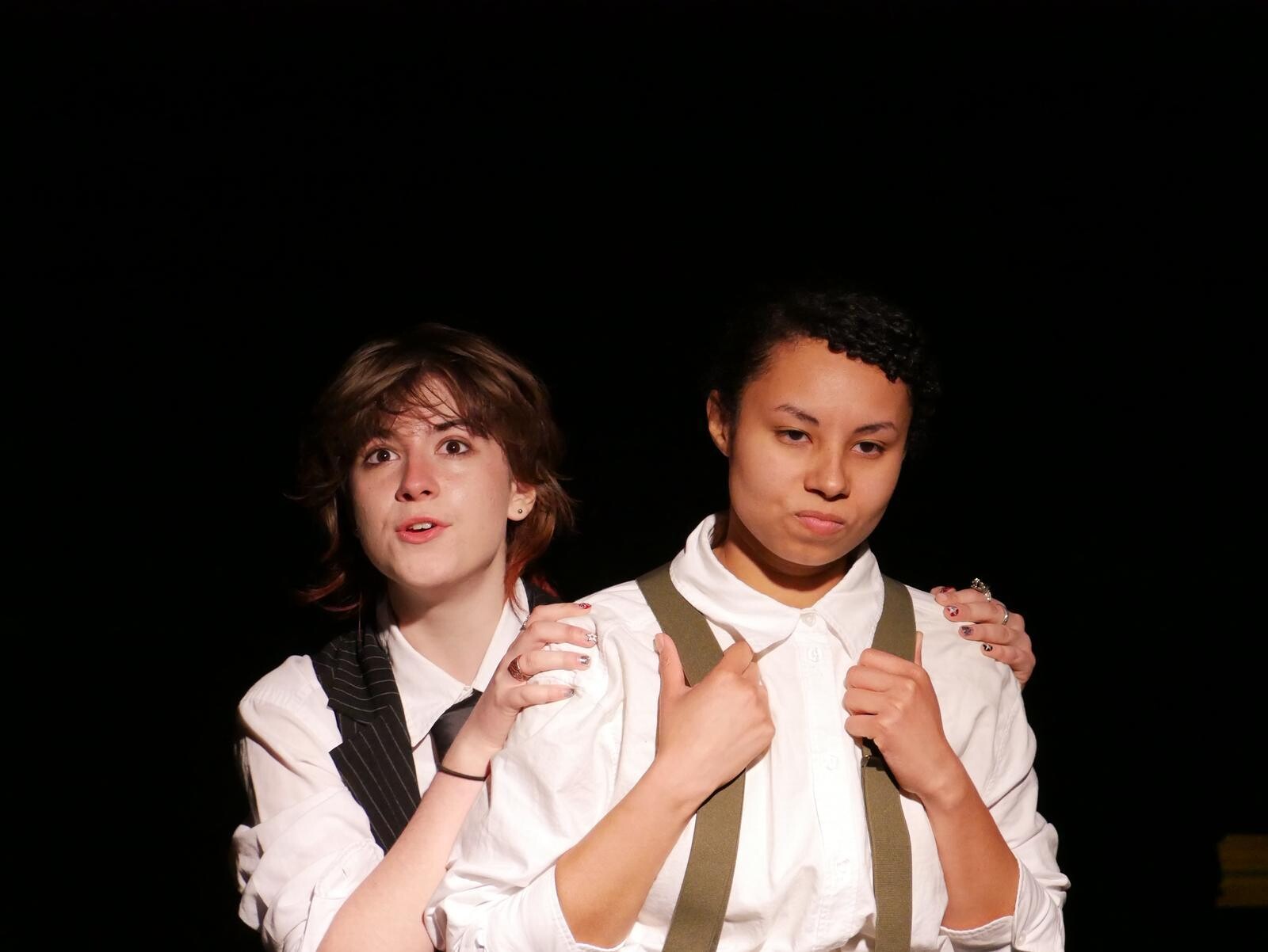Two people on the black stage; the person in the back is holding onto the person in front.
