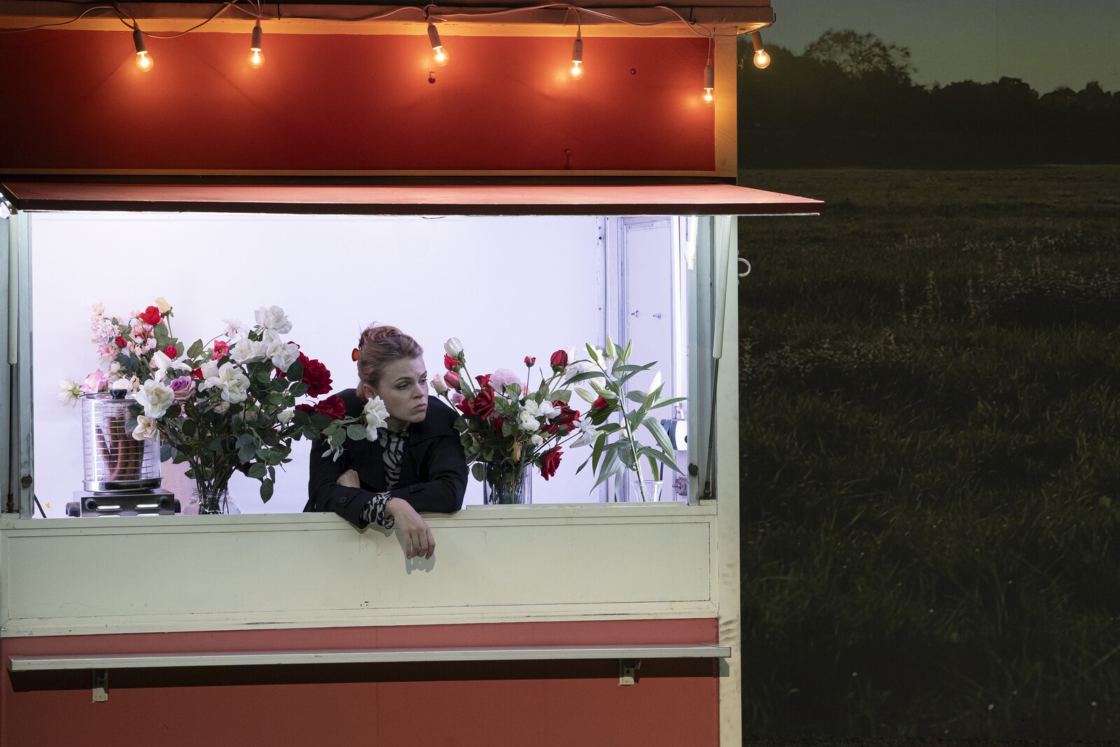 A woman dressed in black in a food truck decorated with flowers looks thoughtful.