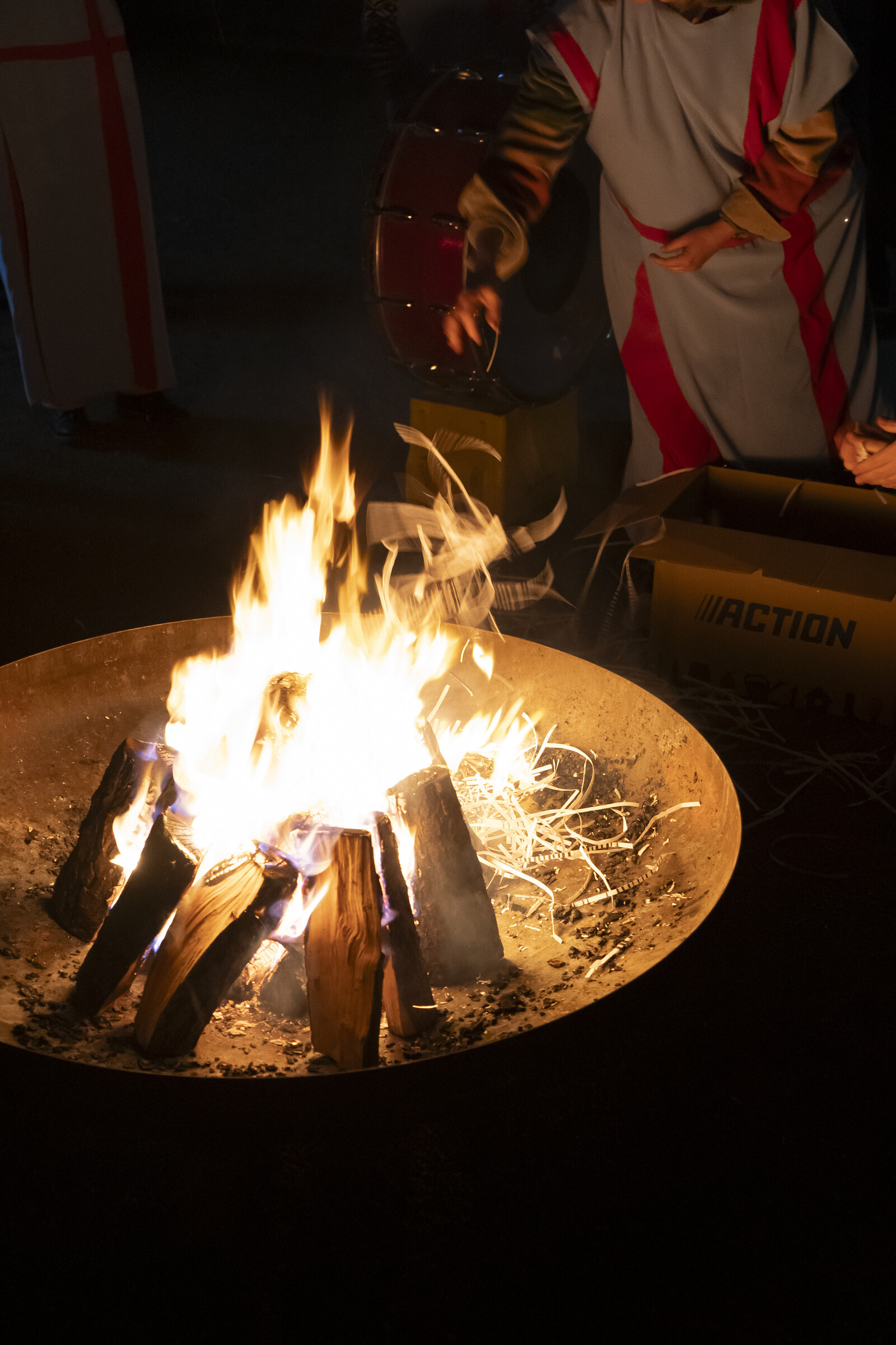 View of a fire into which a person is throwing something.