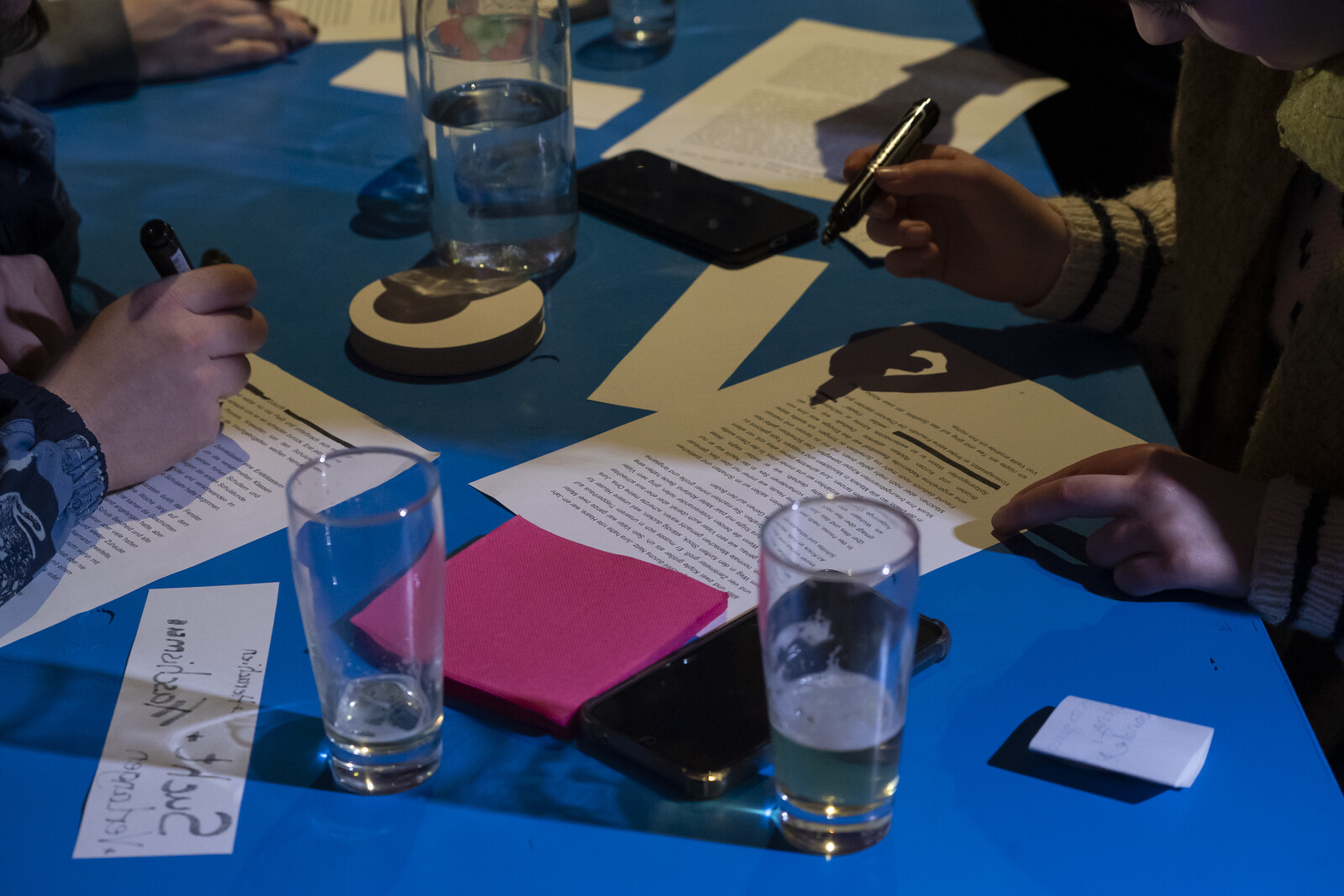 View of a blue table with notes, pens and glasses on which people are writing.